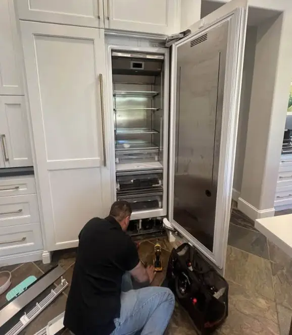 Technician servicing a tall built-in column refrigerator in a white kitchen