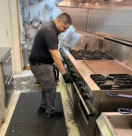 Technician working on a commercial gas range and oven in a restaurant kitchen