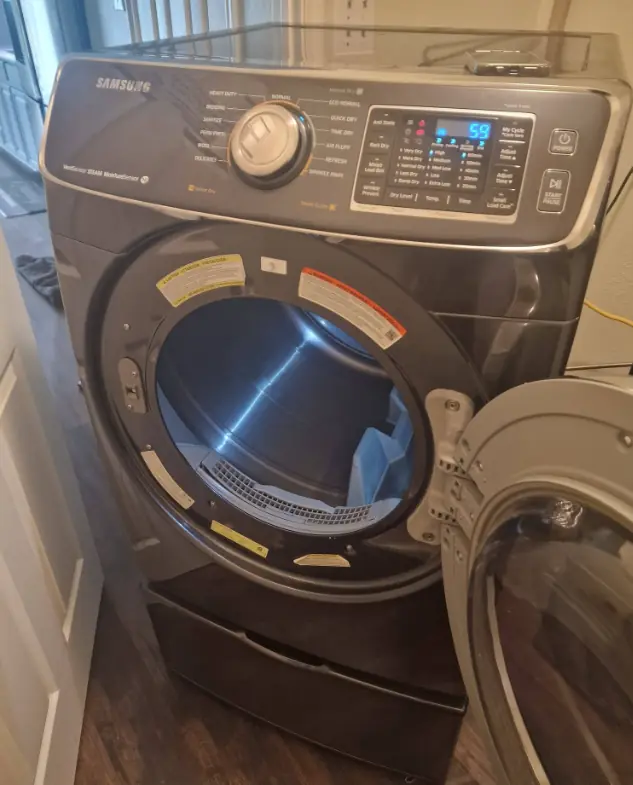 Samsung front-load dryer on a pedestal with the door open for repair